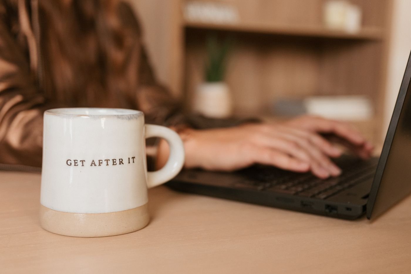 Close-up of a "Get After It" coffee mug beside Kristin's hands typing on a laptop
