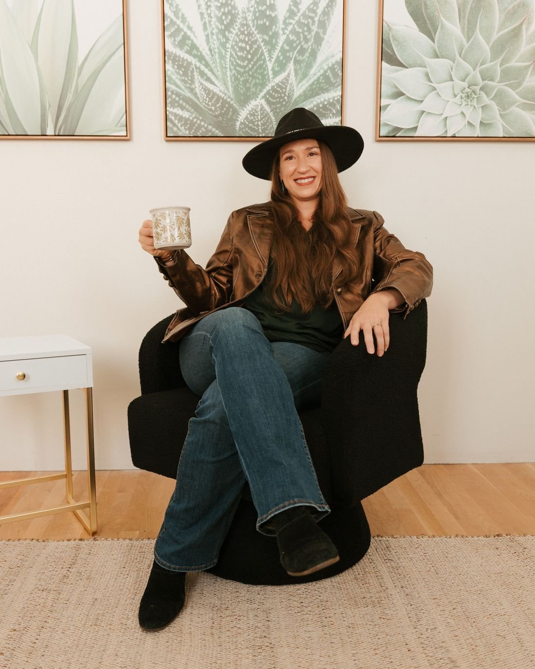Kristin Winstanley relaxing in an armchair, raising a coffee mug in front of succulent artwork