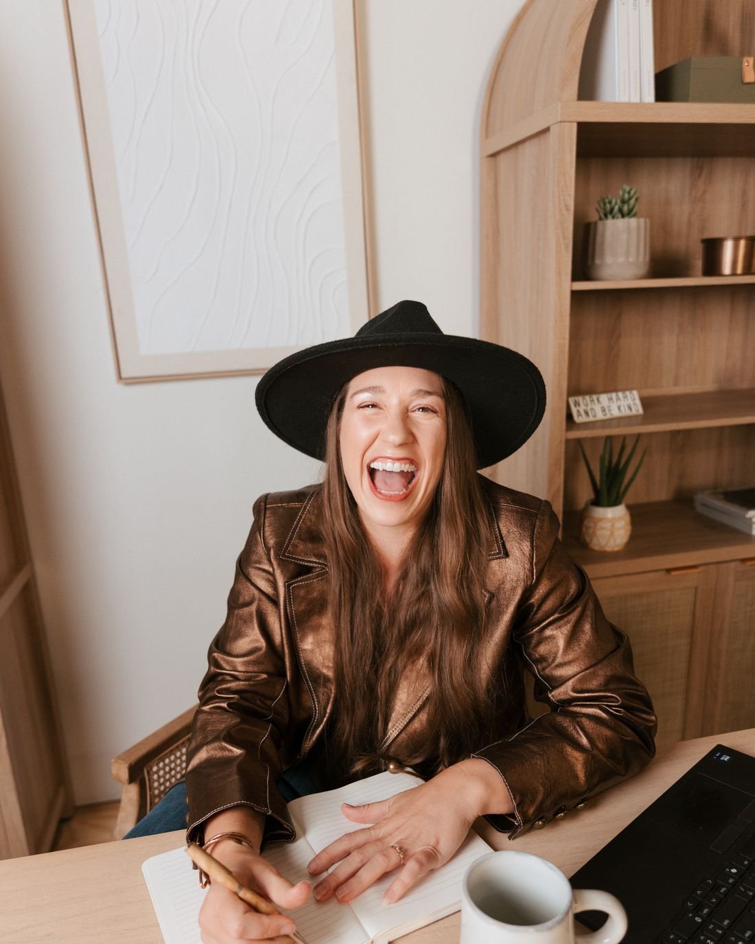 Kristin Winstanley laughing at her desk with a notebook and coffee mug