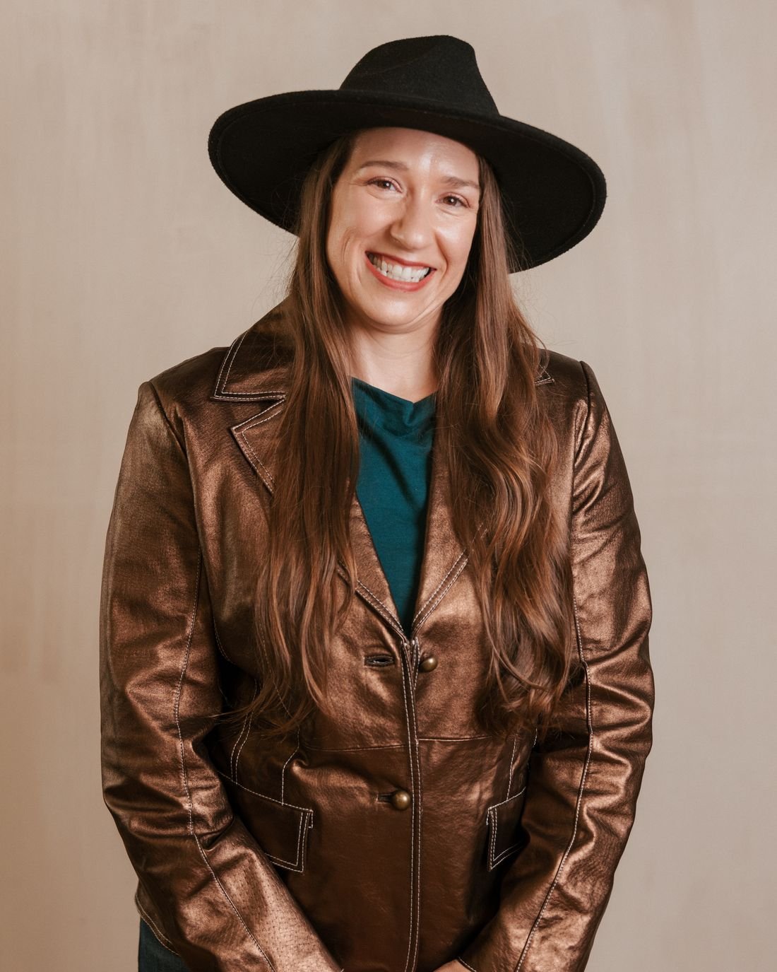 Portrait of Kristin Winstanley, CPA, in a copper leather jacket and black hat